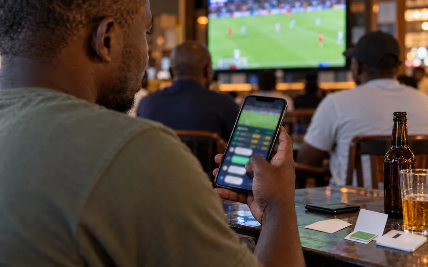 GSB customer care illustrated by a support conversation on a betting phone in a sports bar.