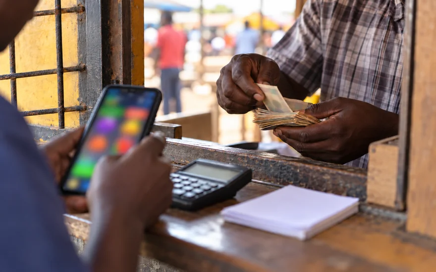 GSB withdrawal illustrated by cash counted at an agent window beside a betting phone.